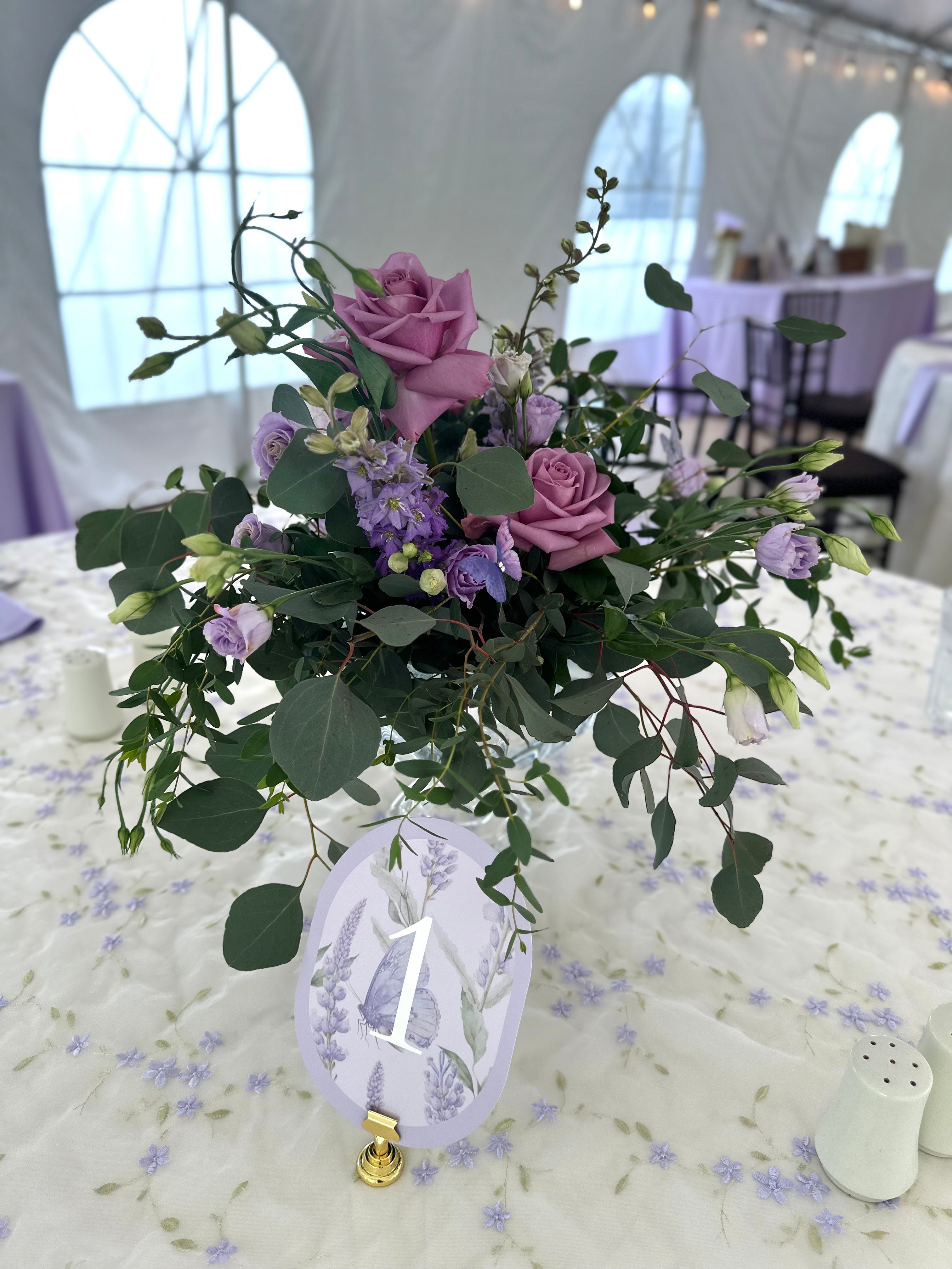 Bella Sera Pittsburgh - Floral arrangement with purple roses and greenery on a tablecloth with a number '1' card.