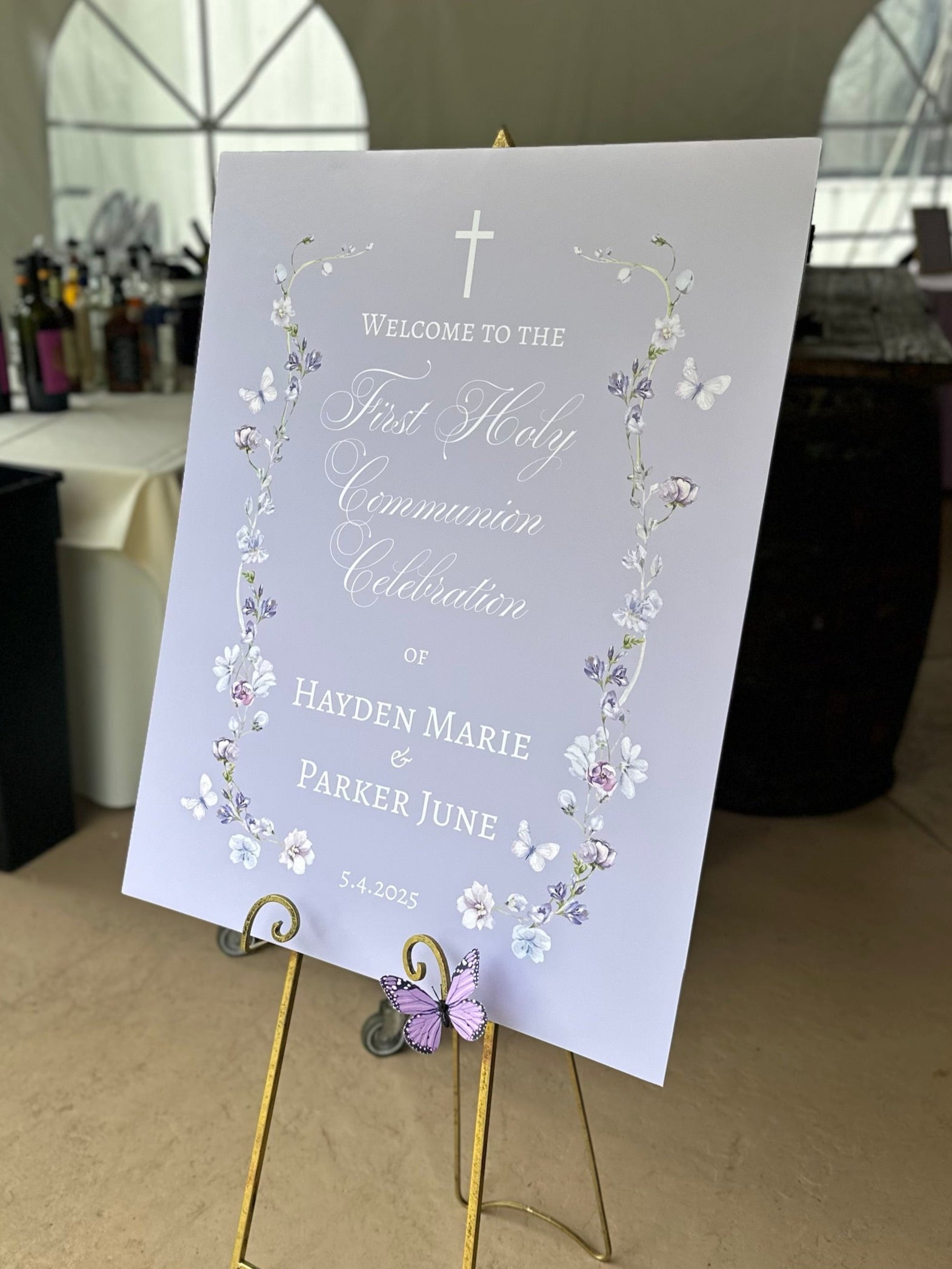 First Holy Communion Celebration sign  on a gold easel with floral design and text, placed indoors.