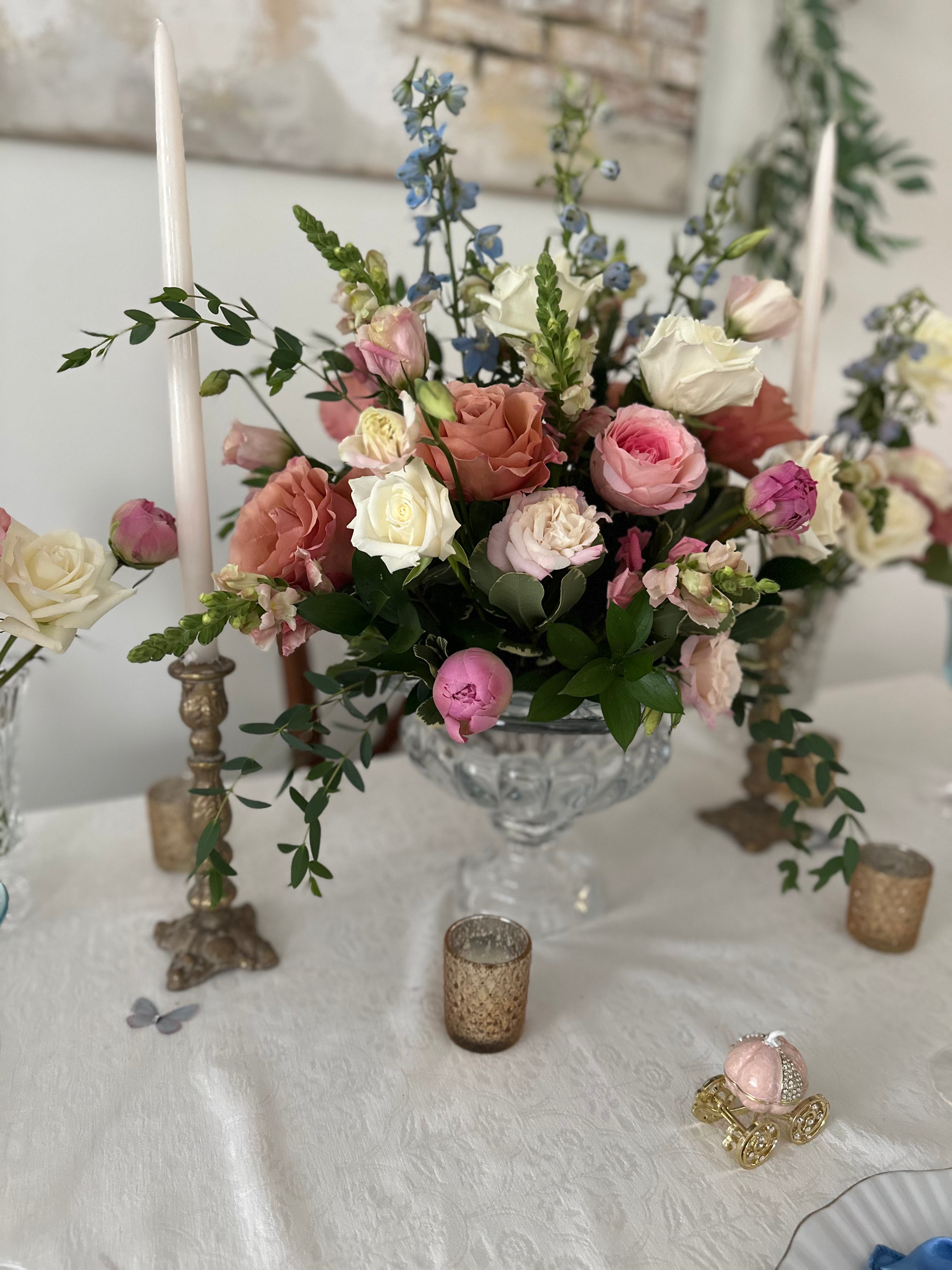 Floral arrangement in a crystal vase on a table with candles and decorative items.